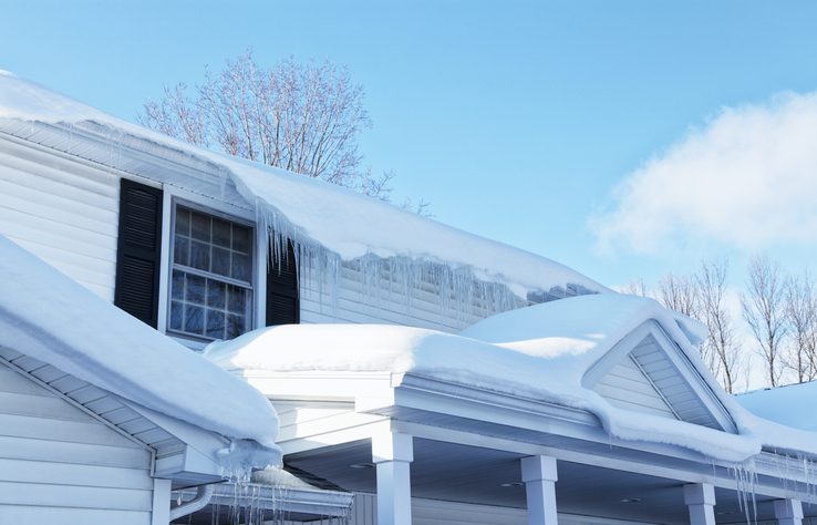 Melting snow and icicles dripping down from the rooftop edges and eavestrough gutters of a residential house roof and front porch. Sunny winter day.